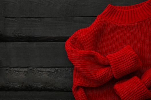 Red knitted sweater on wooden background, top view