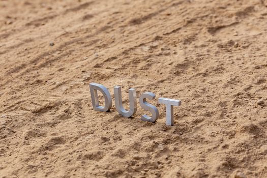 the word dust standing on dusty road surface in linear perspective with selective focus and background blur under direct sunlight