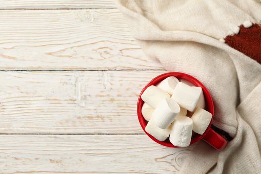 Cup with marshmallows and sweater on wooden background