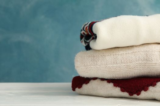 Pile of sweaters on white wooden table against blue background