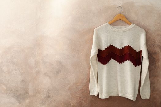 Knitted sweater hanging on a hanger against brown background