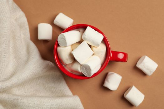 Cup of coffee with marshmallows and sweater on brown background, top view