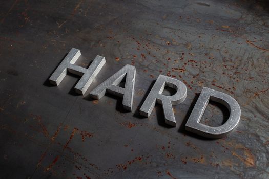 the word hard laid with silver metal letters on rusted burnt iron flat surface background in descending diagonal composition