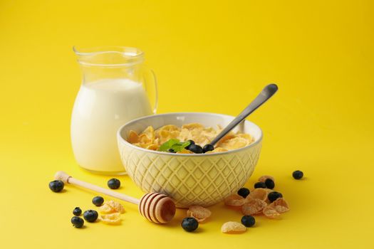 Milk, bowl of muesli and dipper on yellow background