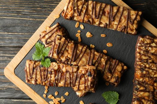 Board with granola bars on wooden background, top view