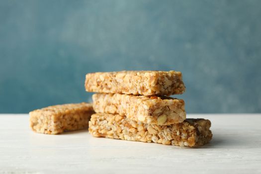 Tasty granola bars on white wooden table against blue background