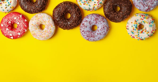 Different tasty donuts on yellow background, top view