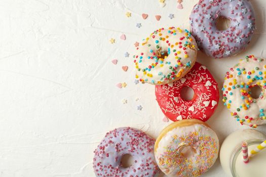 Milk and tasty donuts on white background, top view