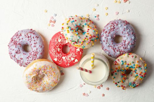 Milk and tasty donuts on white background, top view