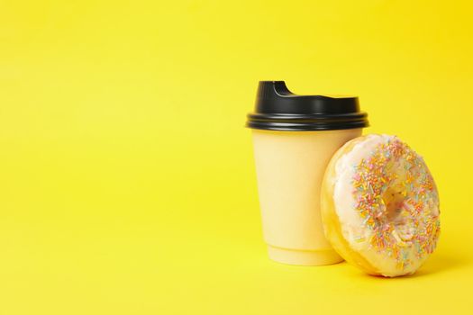 Paper cup and donut on yellow background