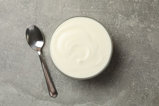 Spoon and bowl of sour cream on gray background, top view