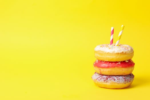 Tasty donuts with straws on yellow background, space for text