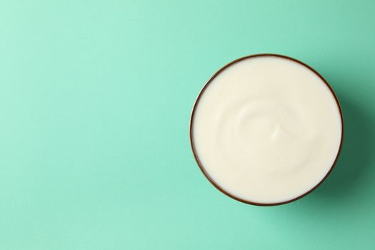 Bowl of sour cream on mint background, top view