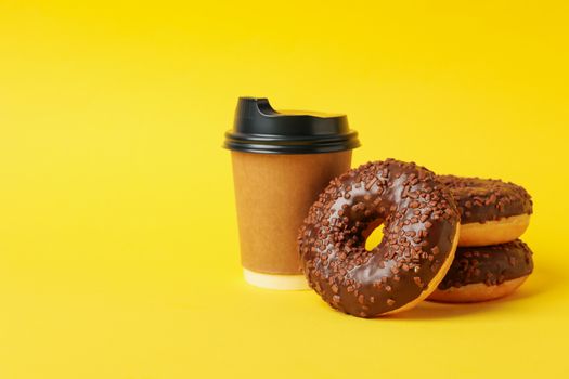 Paper cup and tasty donuts on yellow background