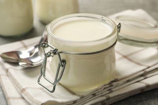 Glass jars of yogurt, spoons and napkin on gray background