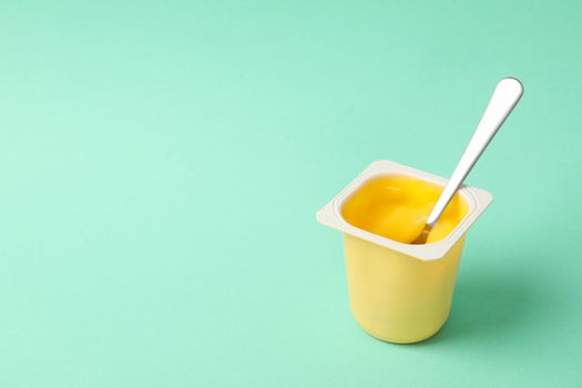 Plastic cup of yogurt with spoon on mint background