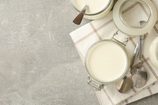 Glass jars of yogurt, spoons and napkin on gray background