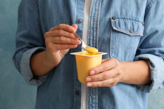 Woman hold plastic cup of sour cream yogurt and spoon against blue background