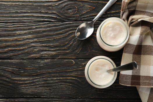 Glass jars of yogurt, spoons and napkin on wooden background