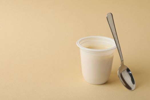 Plastic cup of yogurt with spoon on beige background