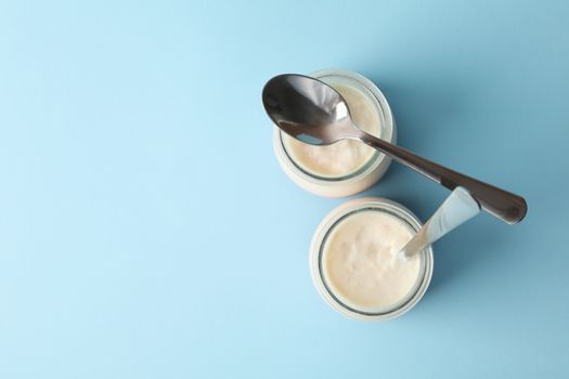 Glass jars of yogurt with spoons on blue background