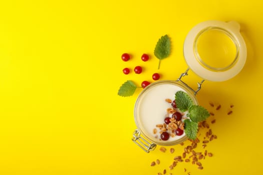 Glass jar of sour cream yogurt with cranberry, mint and granola on yellow background