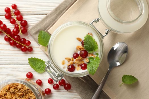 Yogurt with cranberry, granola and mint on white wooden background