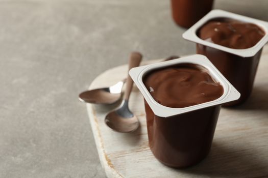 Board with plastic cups of yogurt and spoons on gray background