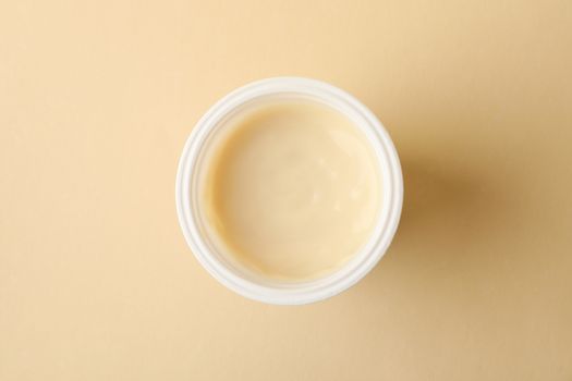 Plastic cup of yogurt on beige background, top view