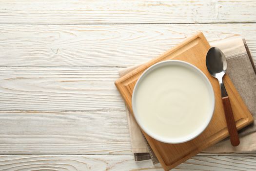 Sour cream yogurt, spoons and napkin on white wooden background