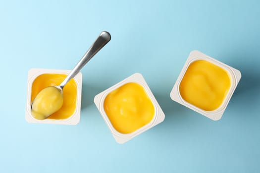 Plastic cups of yogurt and spoon on blue background