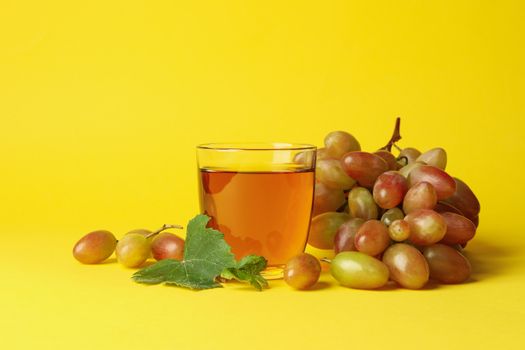 Glass of juice and grape on yellow background