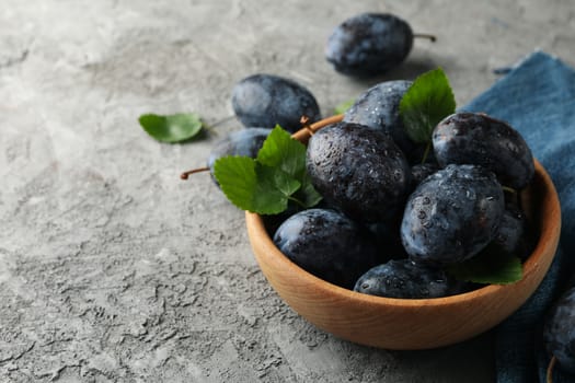 Napkin and bowl with plums on gray background