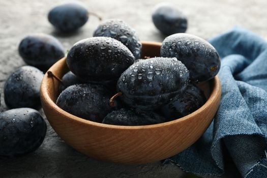 Napkin and bowl with plums on gray background