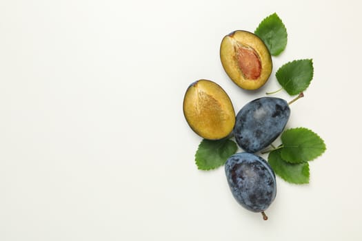 Fresh plums and leaves on white background, top view