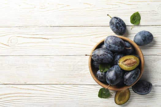 Bowl of plums on wooden background, top view