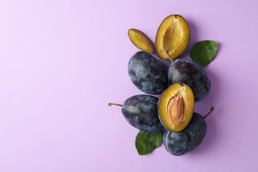 Fresh plums and leaves on violet background, top view