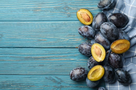 Napkin and fresh plums on wooden background, top view