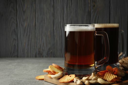 Beer and snacks on gray table against wooden background