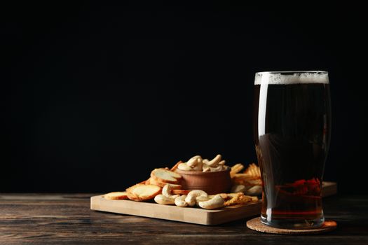 Glass of beer and snacks on wooden table