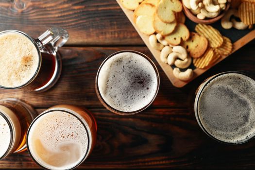 Glasses of beer and snacks on wooden table