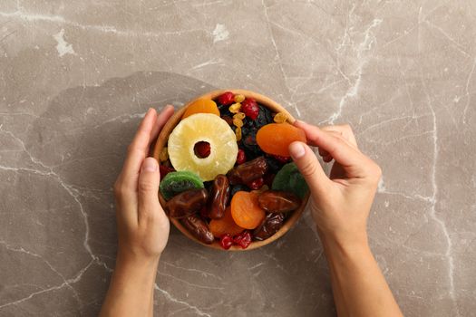 Female hand hold bowl with dried fruits on gray background