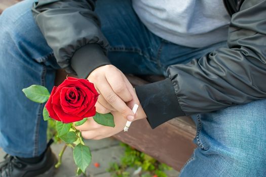 a rose and a cigarette in the hand of a romantic smoking man who is sitting on a bench in the Park, nervous and waiting for a girl