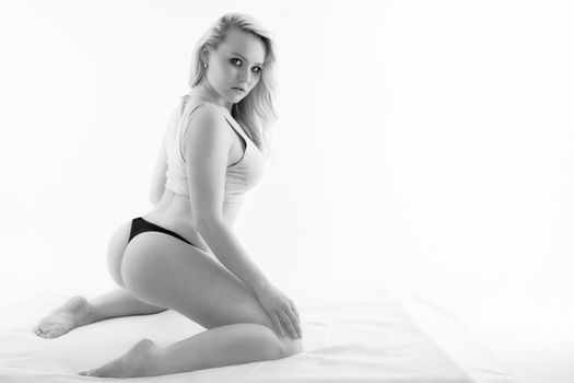 Young blonde woman kneels in the bed