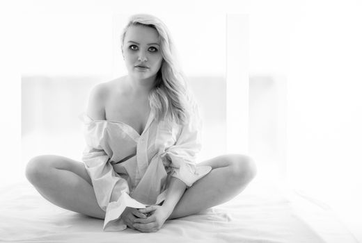 Young blonde woman is sitting in shirt on the bed