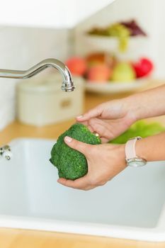 female hands holding broccoli over the sink