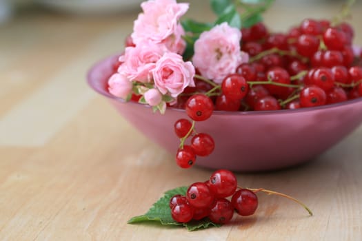 Red currant berries and pink rose blooms in a glass bowl