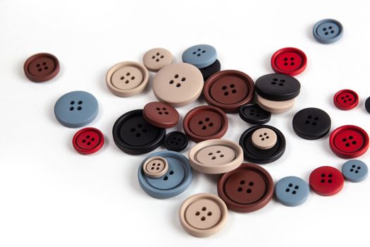 Pile of color brown, beige, grey, red, black plastic matte buttons on white, beautiful needlework, minimalism. Use for sewing. Space for text.