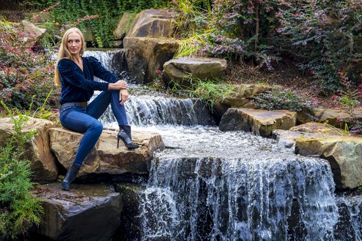 A gorgeous blonde model sits near a waterfall at a local park