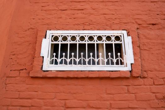 A small white window with bars on the red brick facade.